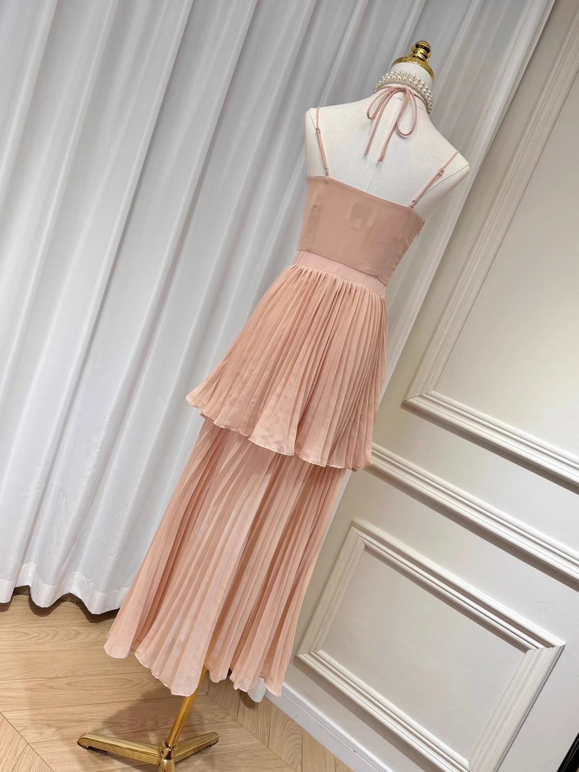 Pink dress on a mannequin against a white curtain background