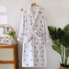 White robe with pink heart patterns hanging on a wooden hanger against a white wall.