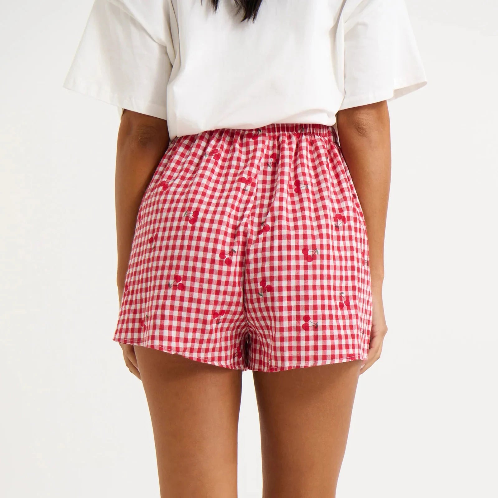 Model displaying red plaid shorts with cherry print and an elastic high waist.