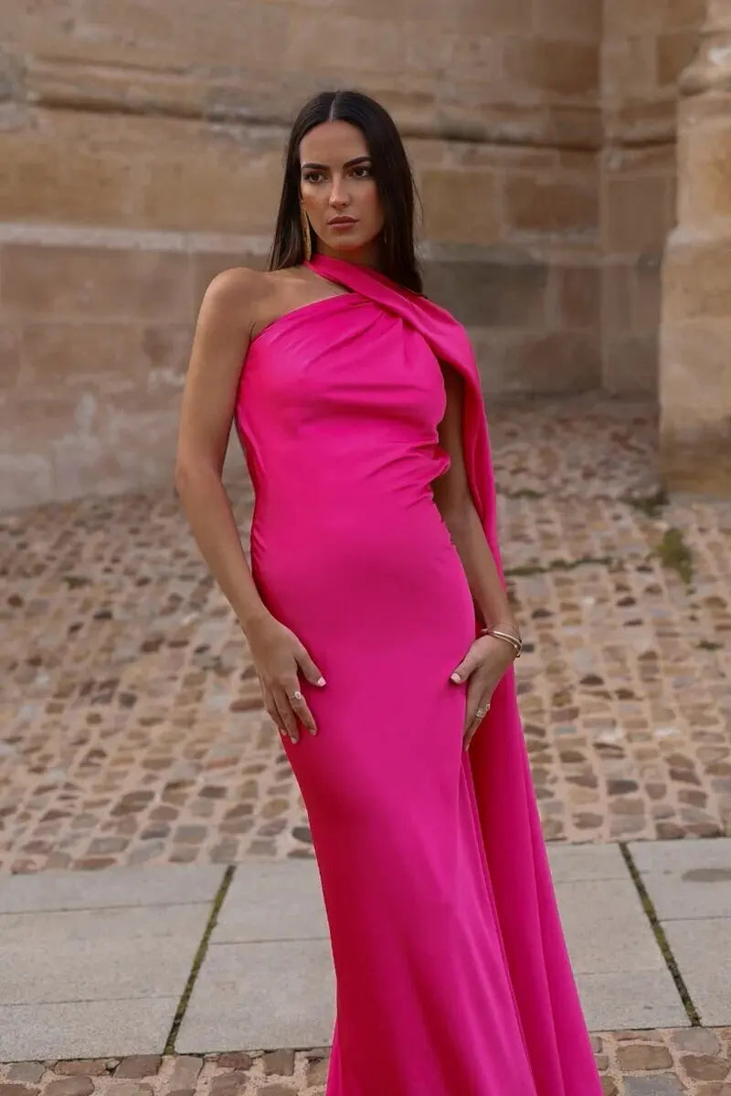 Woman in a bright pink one-shoulder dress standing in front of a stone wall.