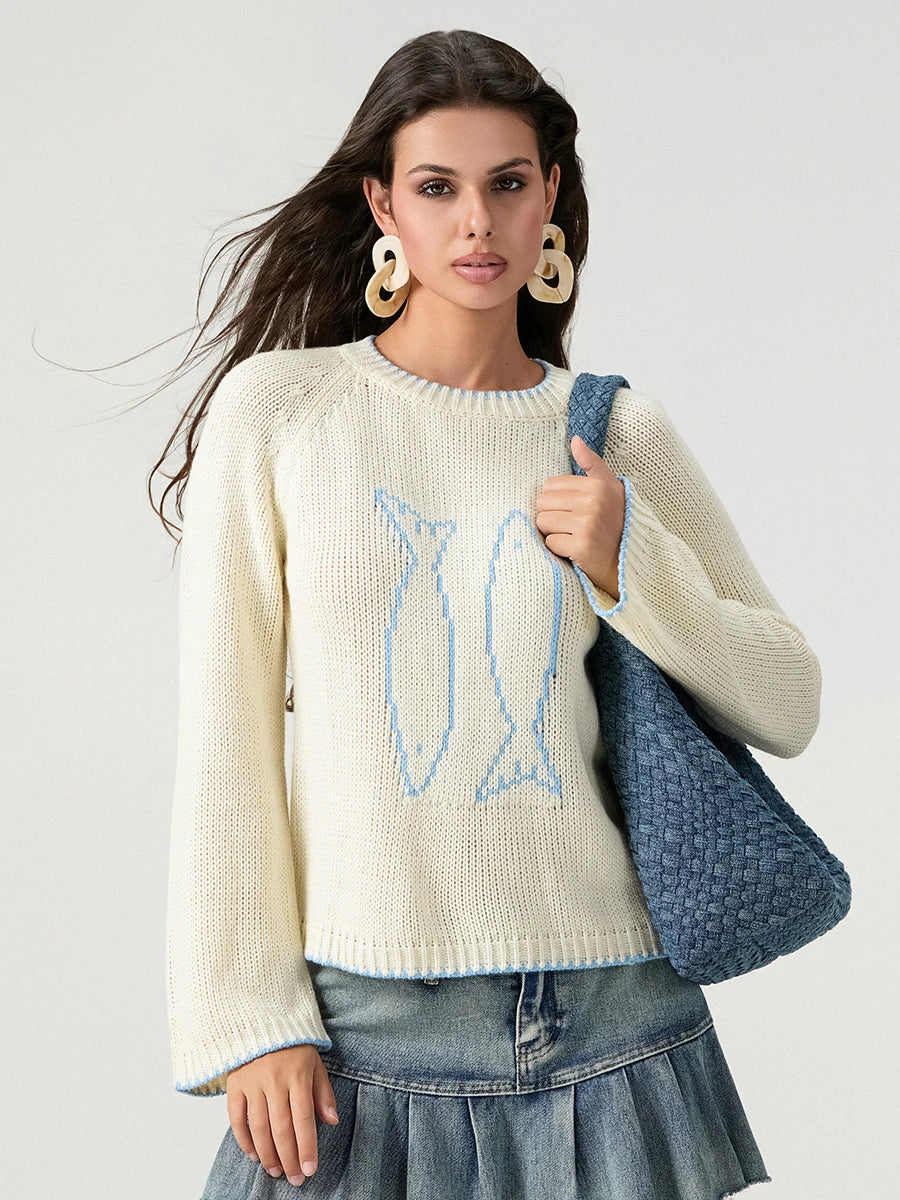 Woman wearing a cream sweater with a blue design, holding a denim bag on a light gray background