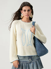 Woman wearing a cream sweater with a blue design, holding a denim bag on a light gray background