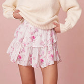 Person wearing a cream sweater and floral skirt on a pink background