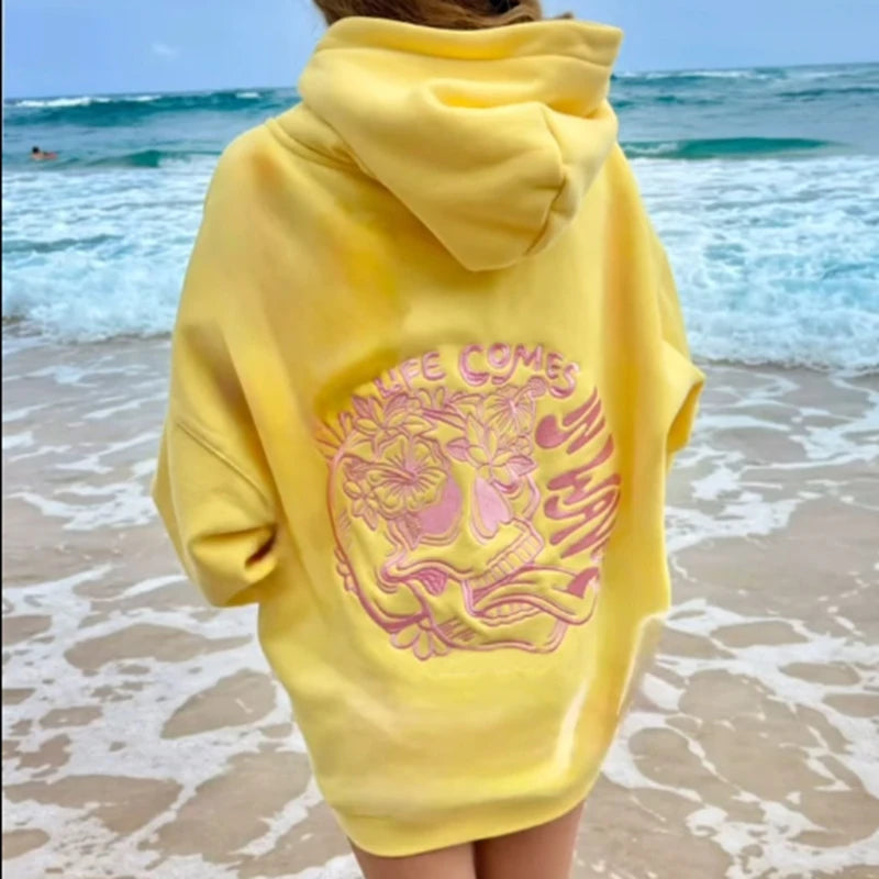 Person wearing a yellow hoodie with a graphic design on a beach