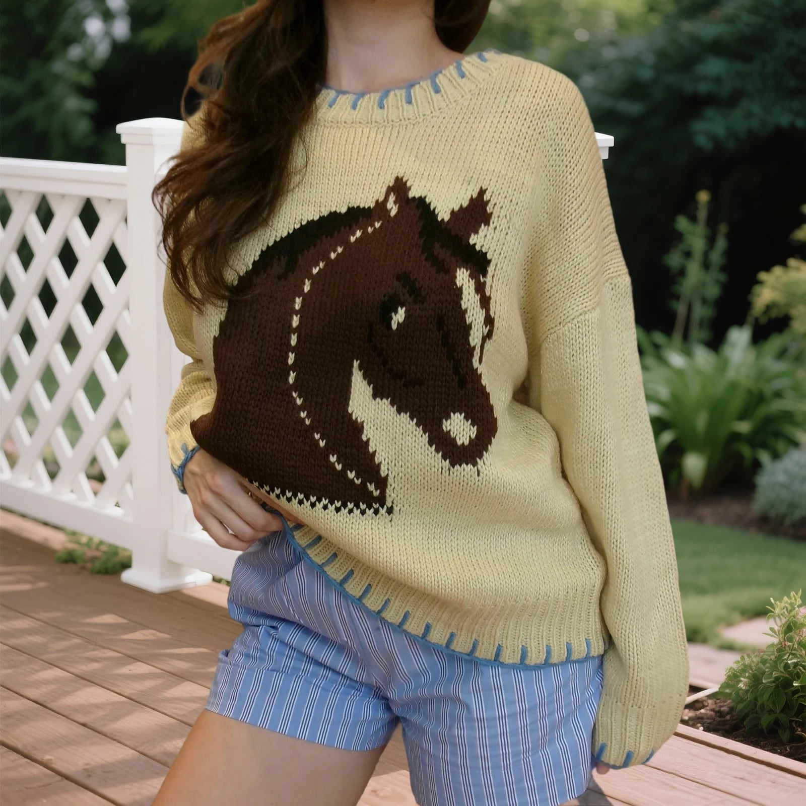 Person wearing a yellow sweater with a horse design outdoors.