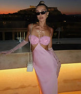 Woman in a pink dress with floral top and cut-out sides standing on a rooftop at dusk.