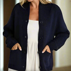Person wearing a navy blue cardigan over a white dress with a neutral background
