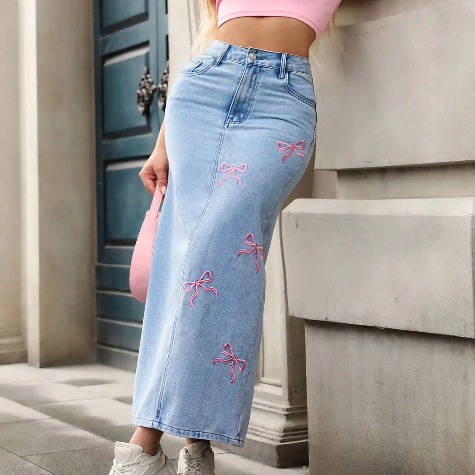 Person wearing light blue jeans with pink bows, standing against a building.