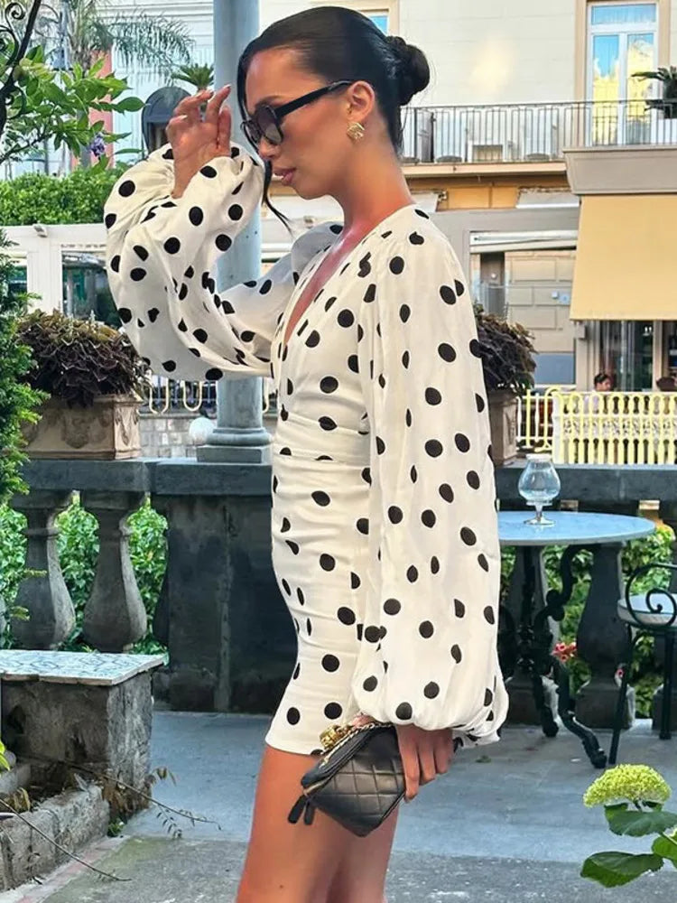 Woman in a polka dot dress standing outdoors with a building and garden in the background