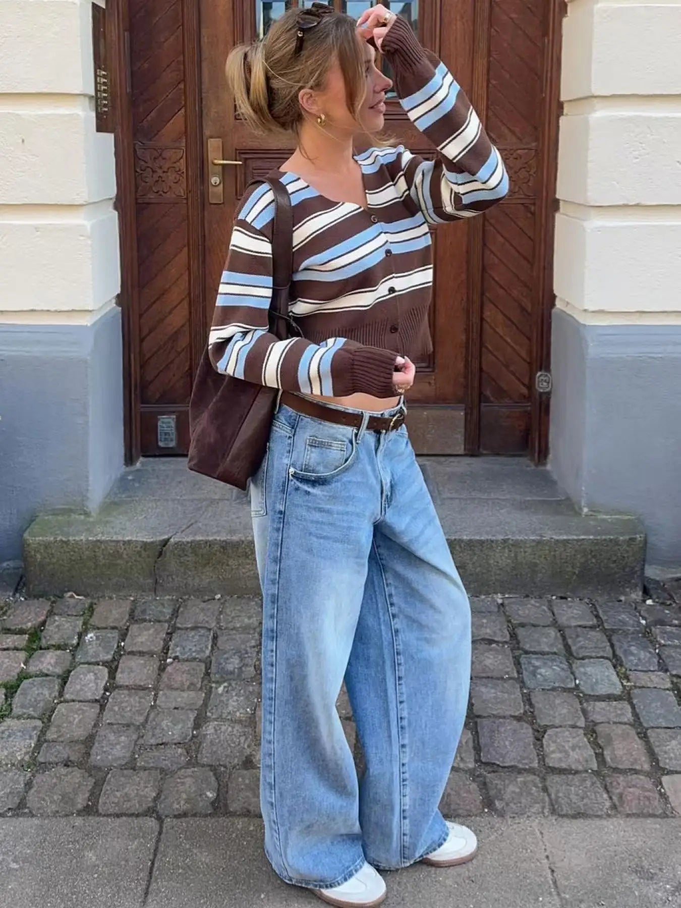 Person wearing a striped sweater and jeans standing in front of a building entrance.