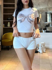 Person wearing a white t-shirt with a bow design and white shorts in an indoor setting.