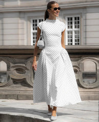 Woman in a white polka dot dress standing in front of a classical building.