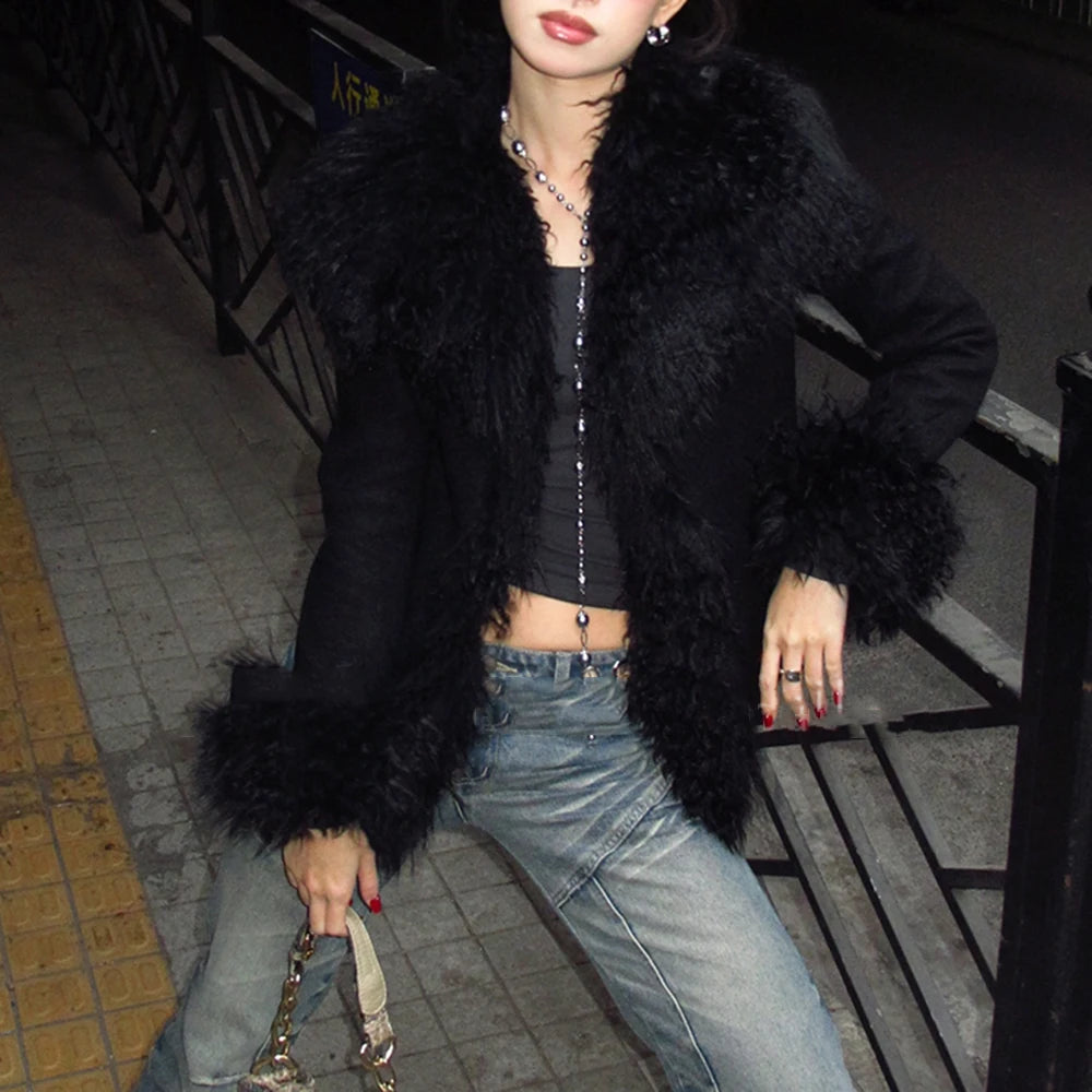 Person wearing a black fur coat and jeans sitting on a bench at night.