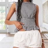 Person wearing a black and white checkered top and white shorts indoors.