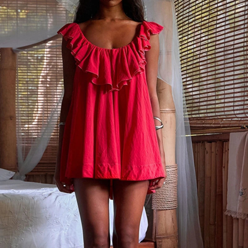Woman wearing a red dress with ruffled details in a bedroom setting.