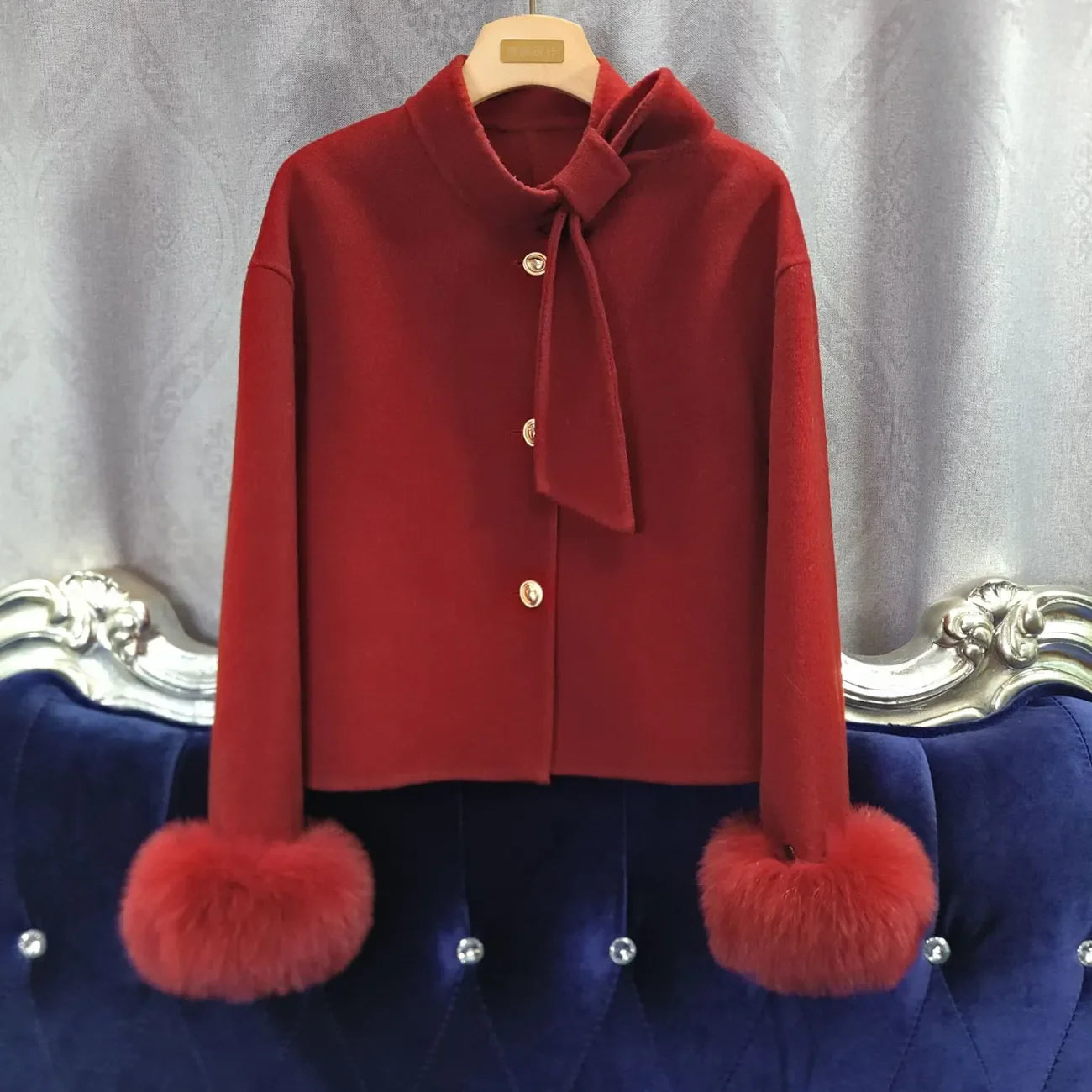 Red jacket with fur cuffs on a hanger against a gray background