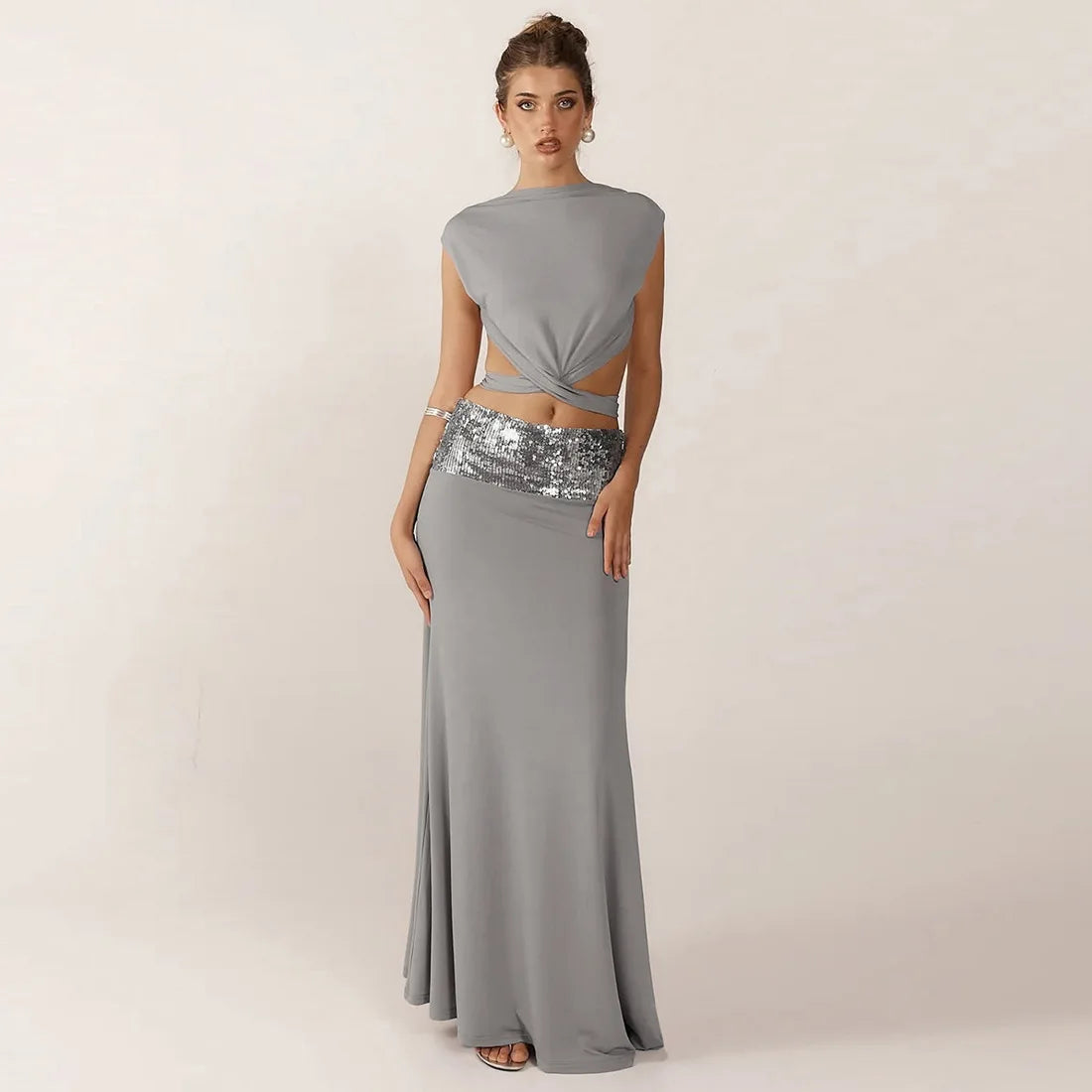 Woman wearing a gray two-piece dress with a sequined waistband on a plain background