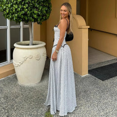 Woman in a white polka dot dress standing outdoors next to a large planter.