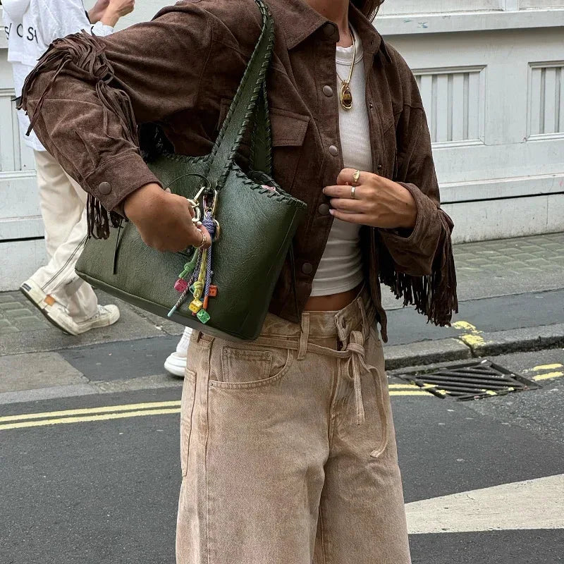 Person wearing a brown jacket with fringes, holding a green bag on a street.