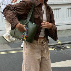 Person wearing a brown jacket with fringes, holding a green bag on a street.