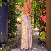 Woman in a floral dress standing in a garden with flowers and plants around.