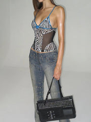 Person wearing a zebra print top and jeans, holding a black studded handbag against a plain background
