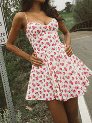 Woman wearing a white dress with red floral pattern standing outdoors.