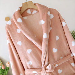 Pink robe with white heart patterns on a wooden hanger against a light background