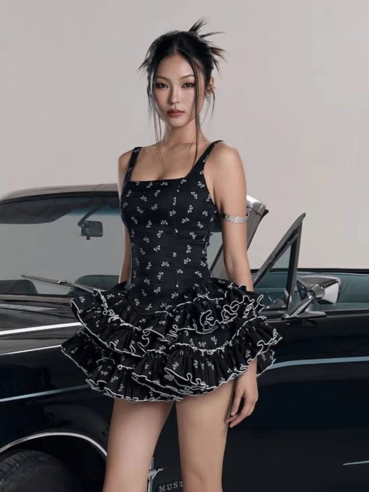 Woman in a black dress with white patterns standing next to a classic car.