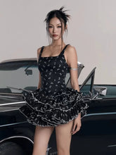 Woman in a black dress with white patterns standing next to a classic car.