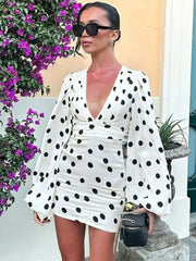 Woman wearing a white polka dot dress with long sleeves in an outdoor setting.