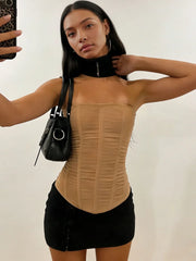 Woman wearing a khaki top and black skirt with a black handbag against a plain background