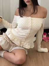 Woman wearing a white off-shoulder top with ruffled details sitting on the floor.