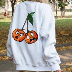 Person wearing a white sweatshirt with cartoon pumpkin cherries on the back in an outdoor setting.