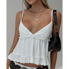 Woman wearing a white lace-trimmed top with a black handbag on a neutral background