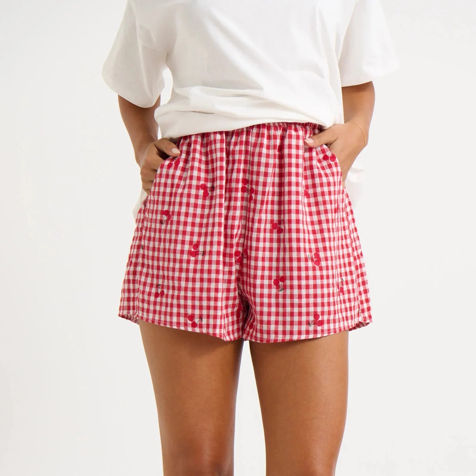 Model displaying red plaid shorts with cherry print and an elastic high waist.
