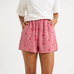 Model displaying red plaid shorts with cherry print and an elastic high waist.