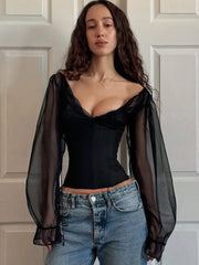 Woman wearing a black top with sheer sleeves and blue jeans against a neutral background