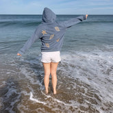 Person wearing a hoodie with shell designs walking on a beach
