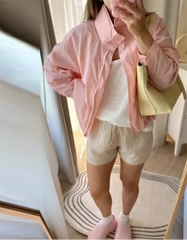 Person wearing a pink jacket and white shorts, holding a yellow bag, standing in front of a mirror.