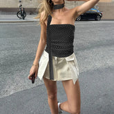Woman in a black polka dot top and beige skirt standing on a street.