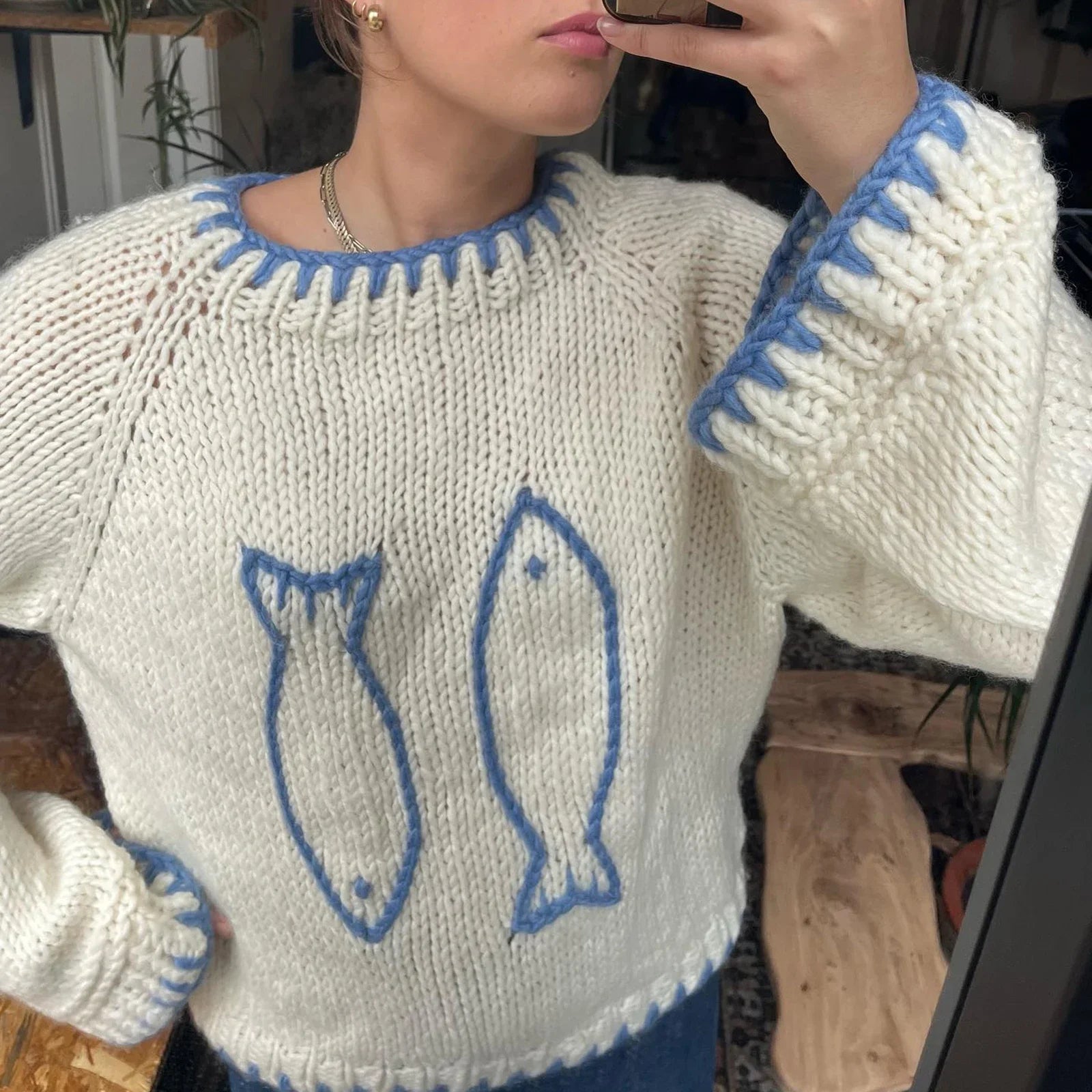 Person wearing a white sweater with blue fish designs, taking a mirror selfie.