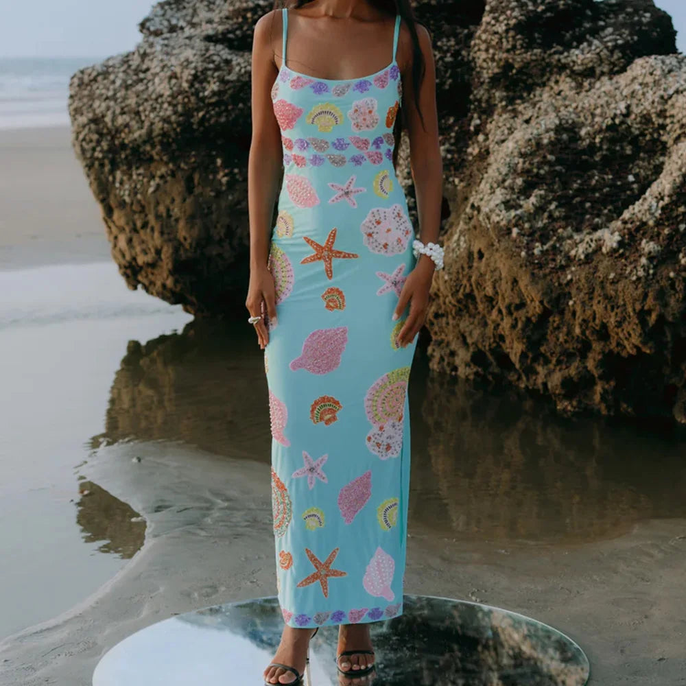 Woman in a floral dress standing on a beach with large rocks.