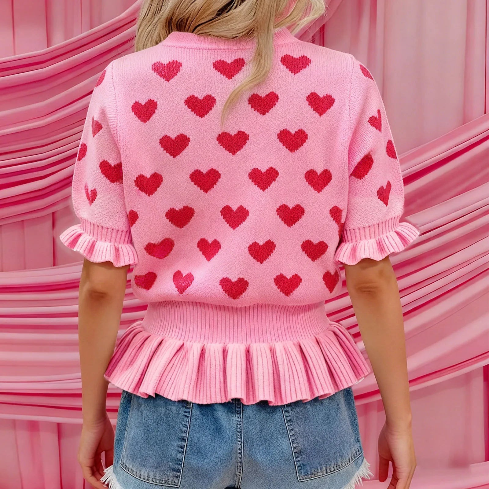 Person wearing a pink sweater with red heart patterns in front of a pink background