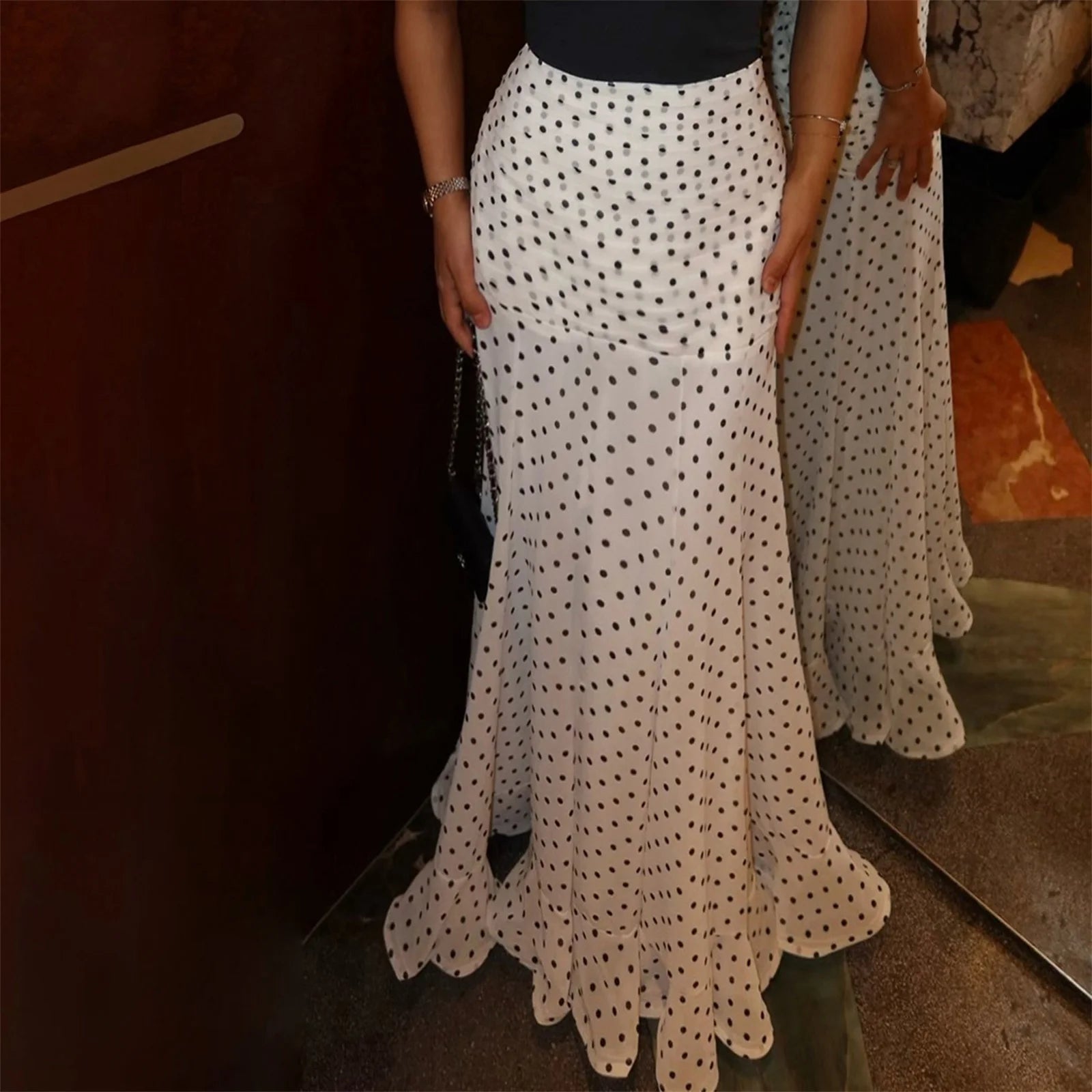 Person wearing a long white polka dot skirt with a dark background