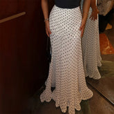 Person wearing a long white polka dot skirt with a dark background