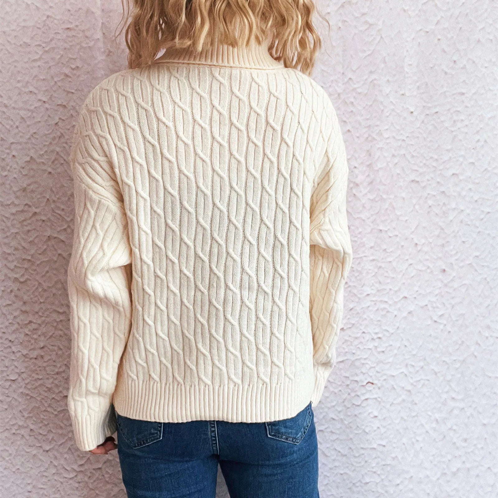 Person wearing a cream cable knit sweater and blue jeans - back view