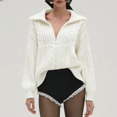 White cable knit sweater with a high collar and black shorts on a plain background