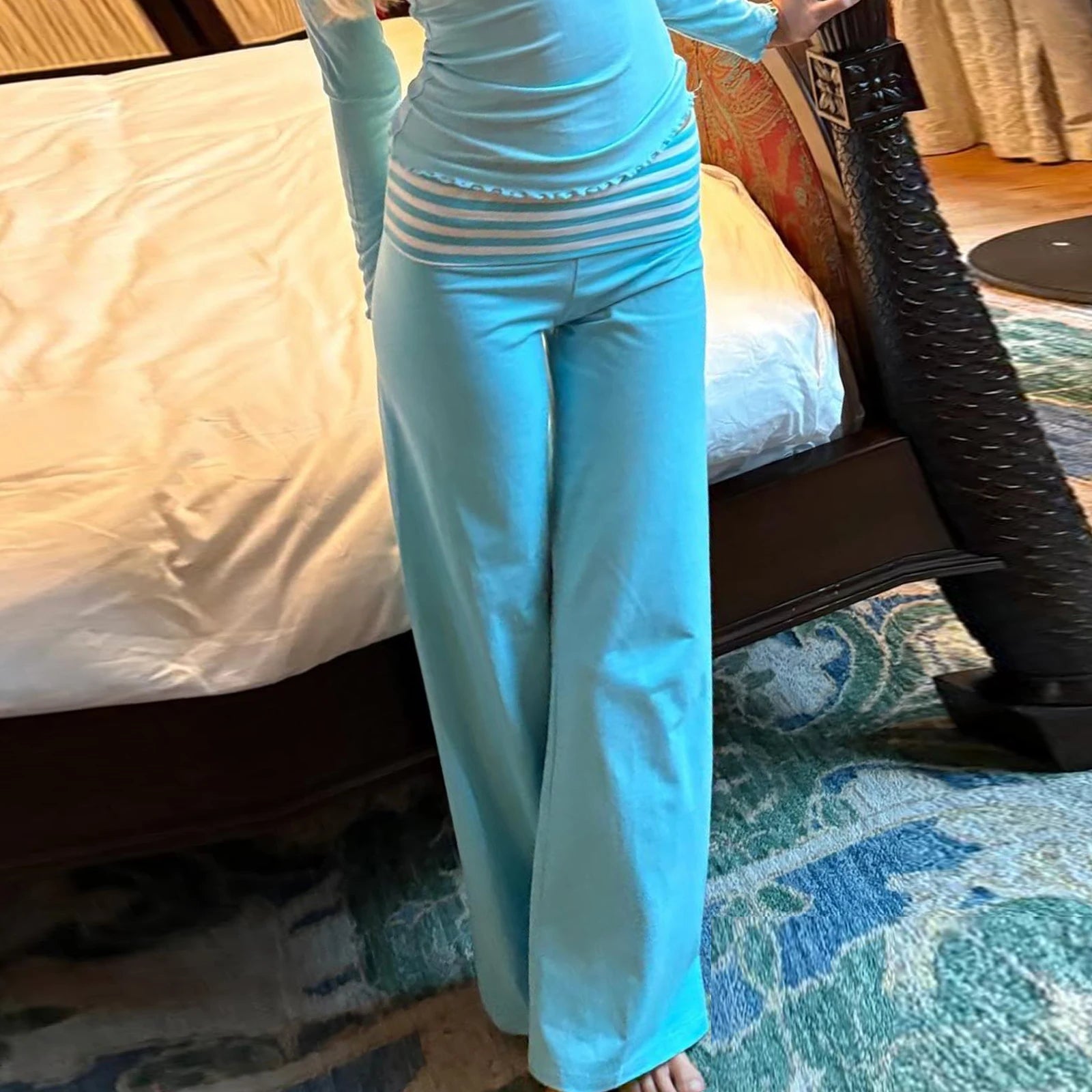Person wearing a light blue outfit with striped top and wide-leg pants in a bedroom setting.