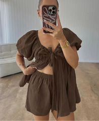 Person wearing a brown outfit with puffed sleeves and a bow detail, standing in a room.